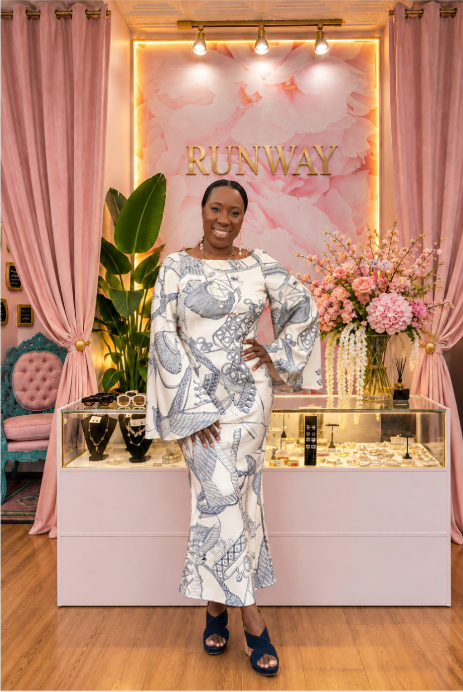A Runway Boutique stylist in a printed cream dress with bell sleeves, standing by the jewelry counter